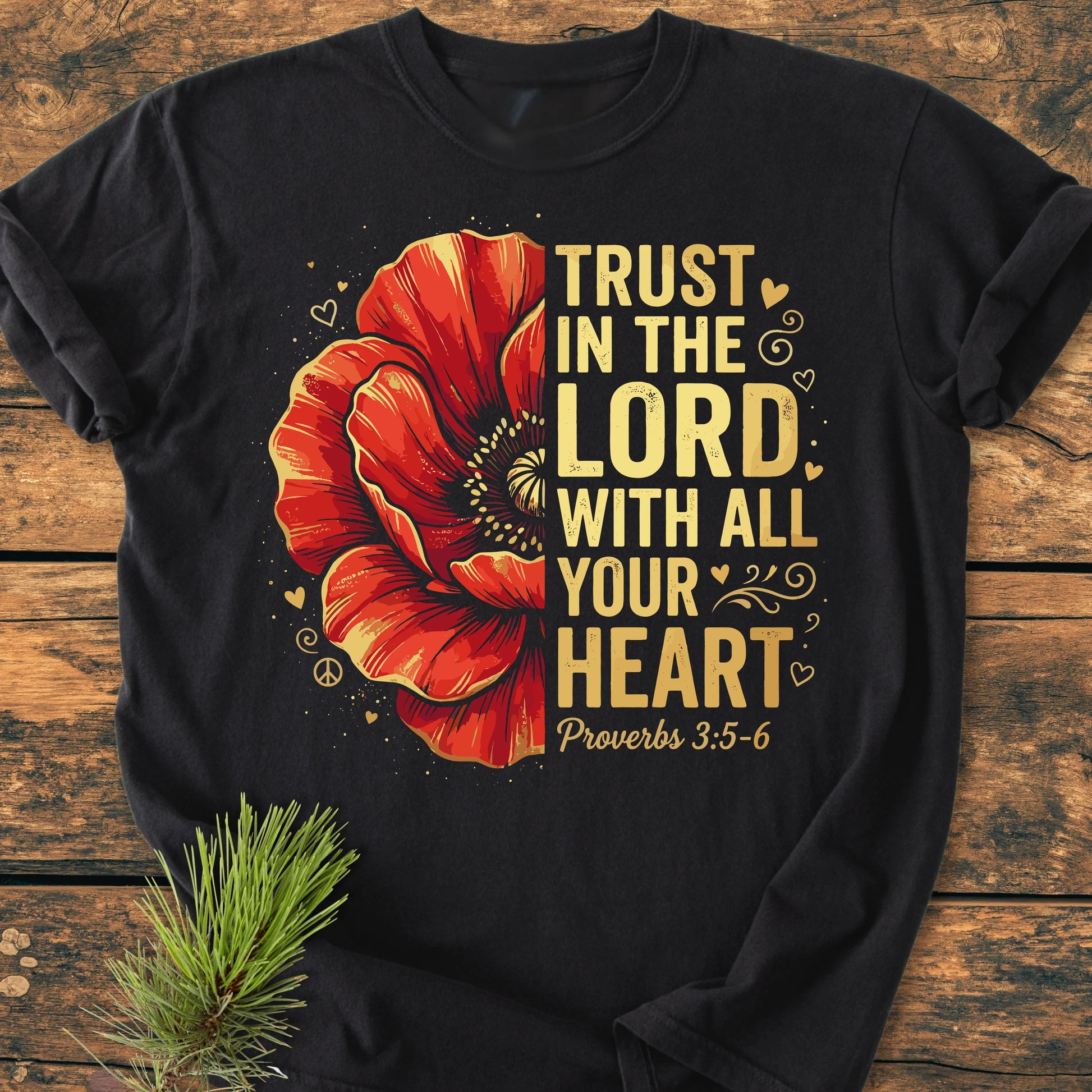Trust In The Lord - Vintage Wash Tee with a red poppy, hearts, and peace sign on left; gold text from Proverbs on right, laid on wooden surface with pine sprig detail.