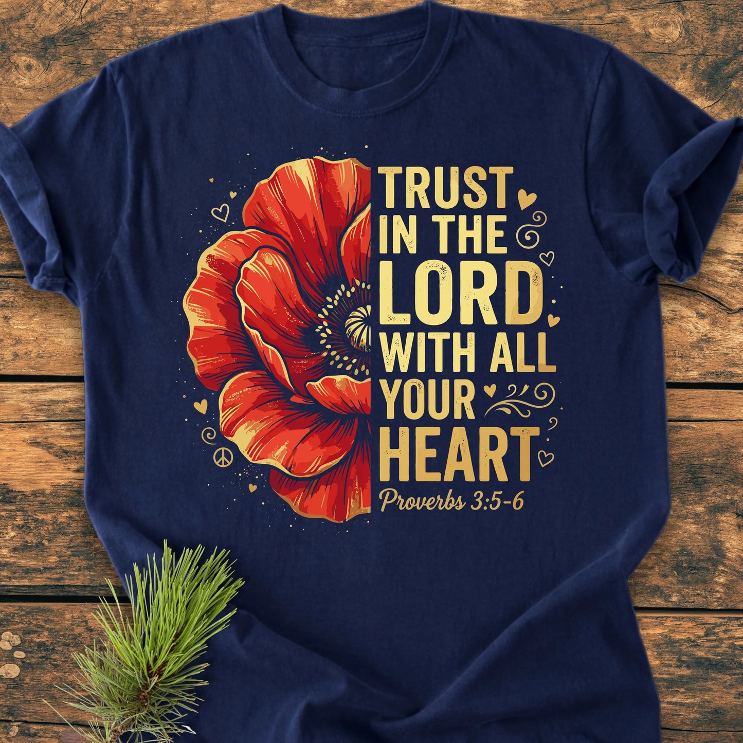 Navy-blue Trust In The Lord - Vintage Wash Tee featuring a red poppy design and gold religious text, displayed on wood with pine sprig, embodying a relaxed vintage fit and feel.