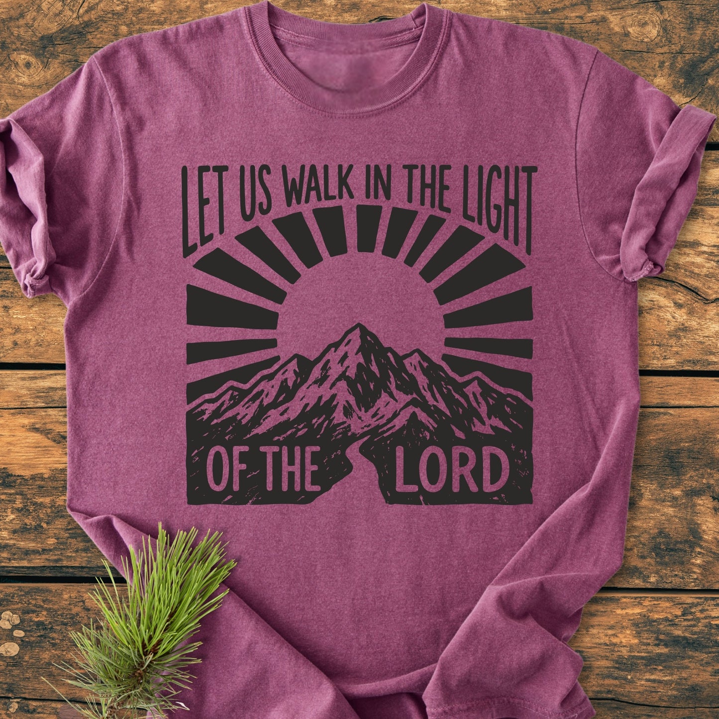 Let Us Walk In The Light Of The Lord - Vintage Wash Tee: A folded purple/magenta T-shirt with mountain graphic and quote, laid on wood, features a cozy, garment-dyed fabric and relaxed fit.