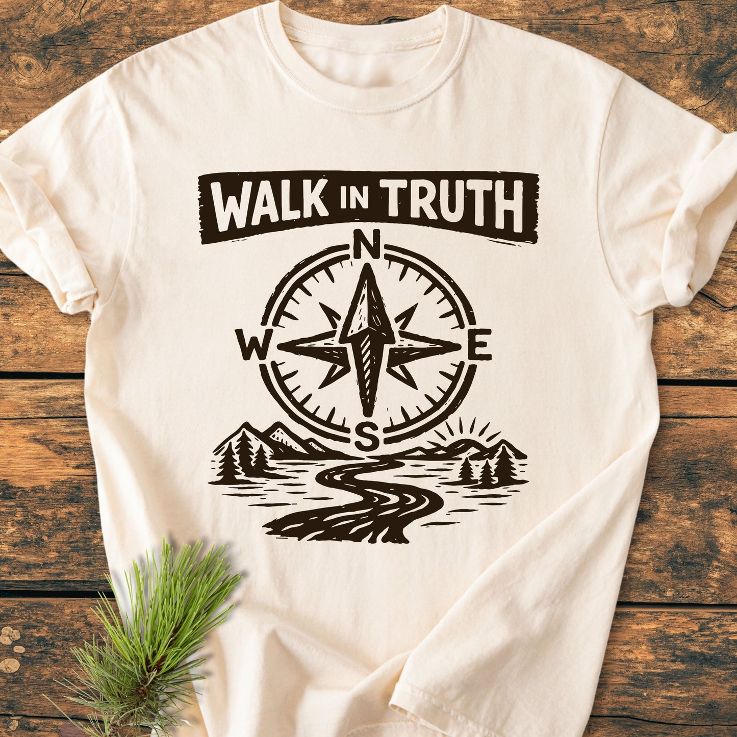 Walk In Truth 3 John 1,4 - Vintage Wash Tee featuring a hand-drawn compass, river, and mountains design, symbolizing guidance, laid on wood with a pine sprig, showcasing its rustic, inspirational style.