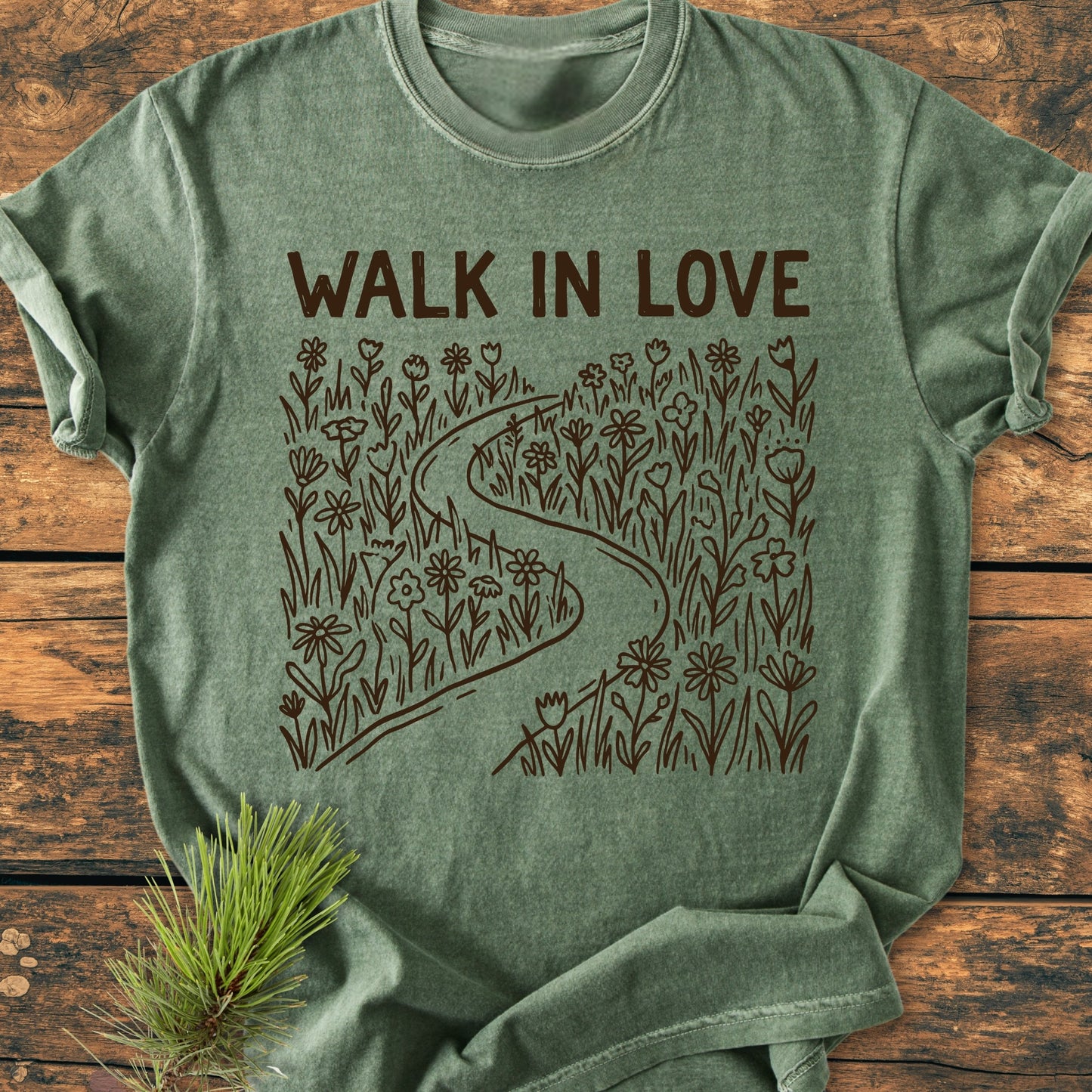 Walk In Love - Vintage Wash Tee, heather-green with WALK IN LOVE and a path drawing, displayed on wood. Includes a pine sprig for natural styling. Relaxed fit, 100% ring-spun cotton.