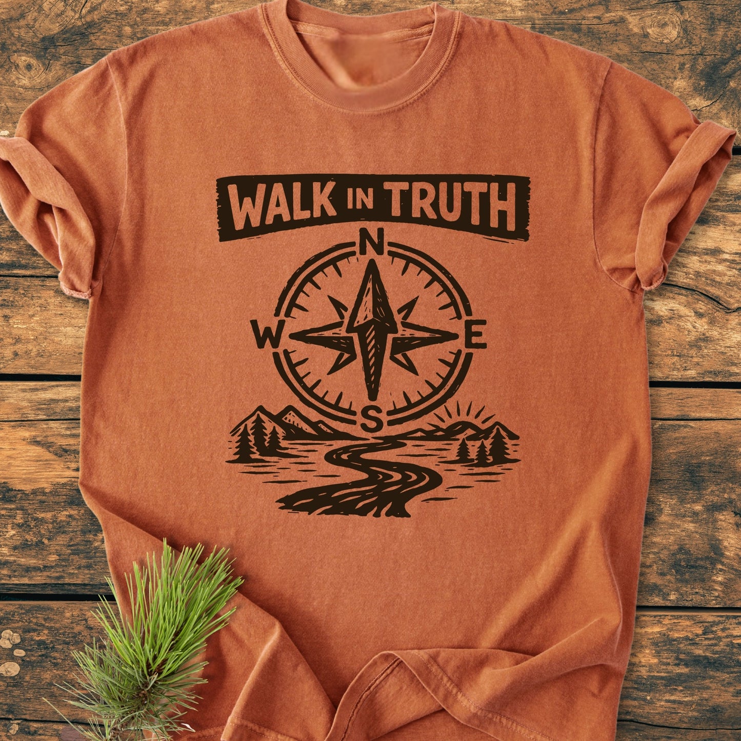Walk In Truth 3 John 1,4 - Vintage Wash Tee features bold text, compass, path, and mountains graphic on an orange-brown shirt, displayed flat with a pine sprig on wood.