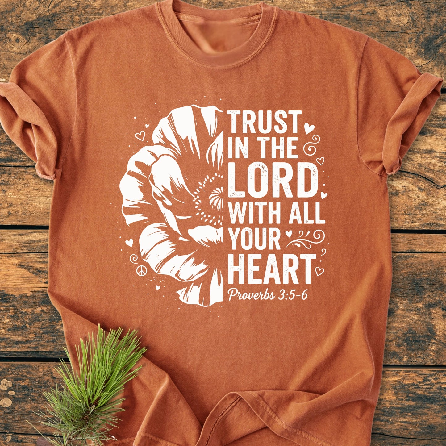 Trust In The Lord - Vintage Wash Tee features a half-bloom flower and biblical text, laid flat with decorative elements. A pine sprig accentuates its soft, relaxed unisex fit.