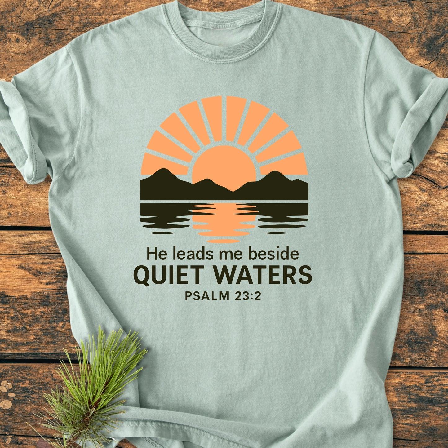 1424 He Leads Me T-shirt features a sun-mountain graphic with Psalm 23:2 text, laid flat; vintage wash, soft, relaxed fit, double-needle stitching, perfect for outdoor enthusiasts and everyday comfort.