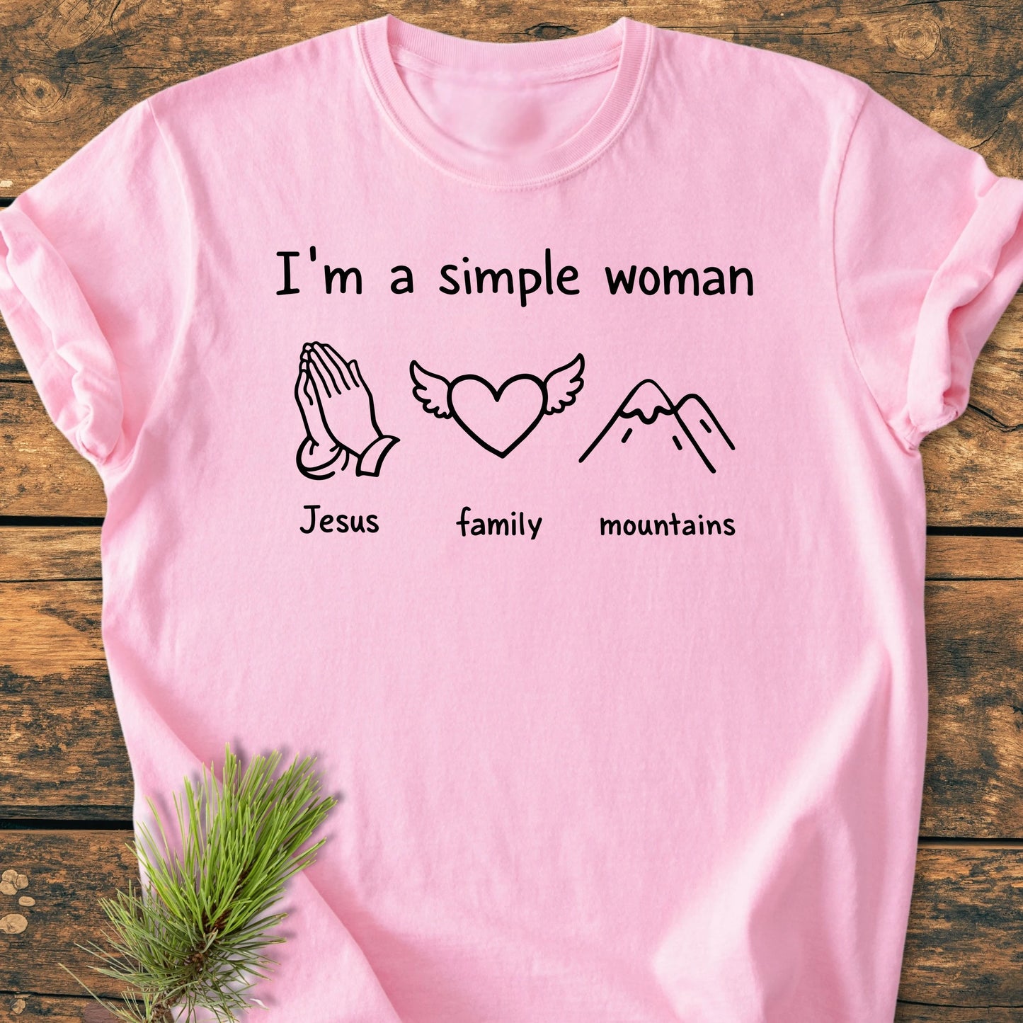 Pink T-shirt on wood with I'm a simple woman phrase above icons: praying hands Jesus, heart family, mountains mountains. Vintage wash, soft, relaxed fit.
